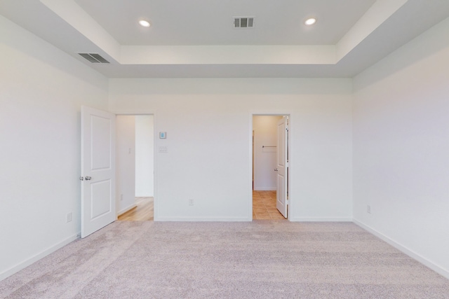 unfurnished bedroom with light colored carpet, a tray ceiling, and a spacious closet