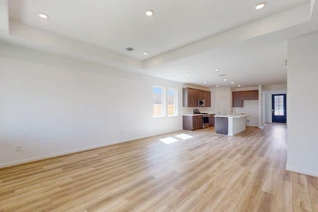 unfurnished living room featuring light wood-type flooring and a tray ceiling