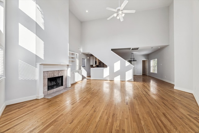 unfurnished living room with high vaulted ceiling, light hardwood / wood-style floors, a tile fireplace, and ceiling fan