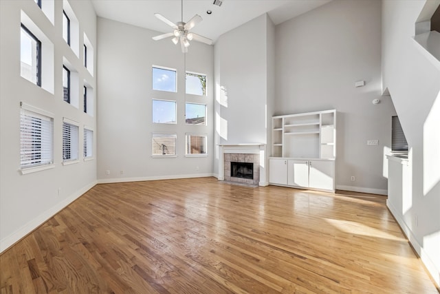 unfurnished living room with ceiling fan, light wood-type flooring, a tiled fireplace, and a high ceiling