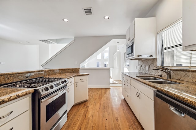 kitchen featuring appliances with stainless steel finishes, white cabinetry, light hardwood / wood-style flooring, dark stone counters, and sink