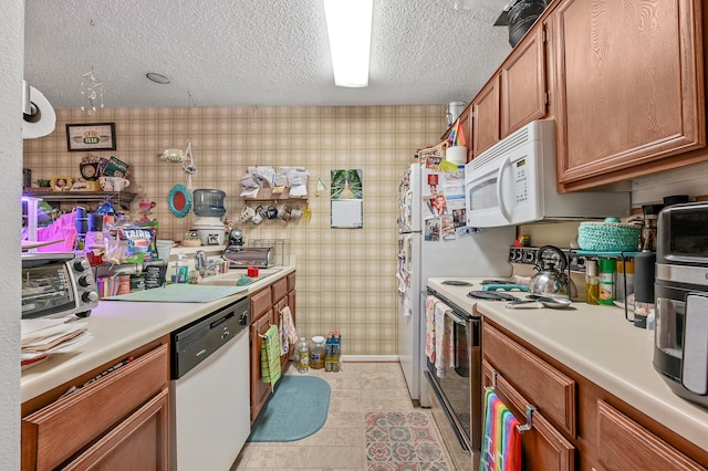 kitchen with a textured ceiling, white appliances, and sink