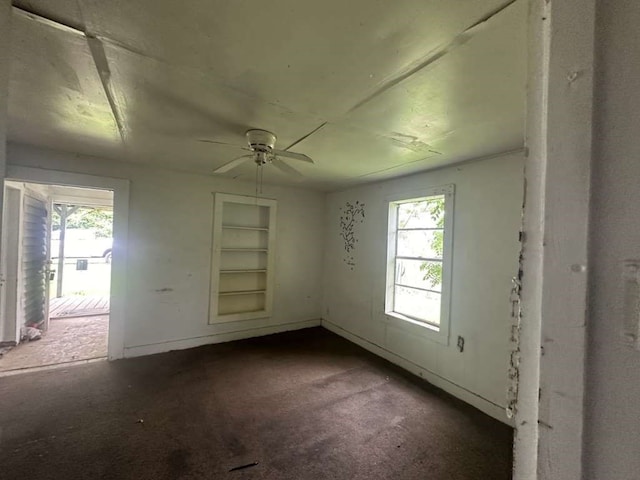 spare room with ceiling fan, built in shelves, and dark carpet