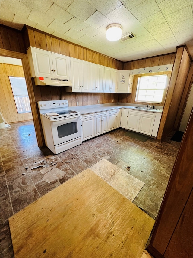 kitchen with white electric range oven, sink, wooden walls, and white cabinetry