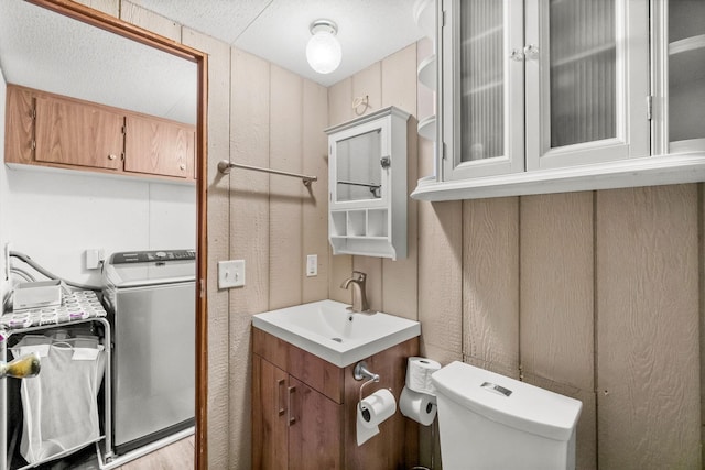 bathroom featuring vanity, washer / clothes dryer, wooden walls, and toilet