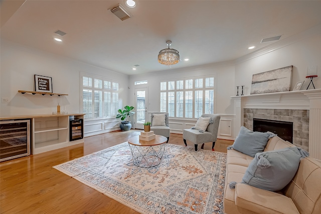 living room featuring a wealth of natural light, wine cooler, light wood-type flooring, and a stone fireplace