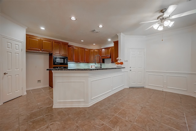 kitchen featuring ceiling fan, ornamental molding, kitchen peninsula, dark stone countertops, and black microwave