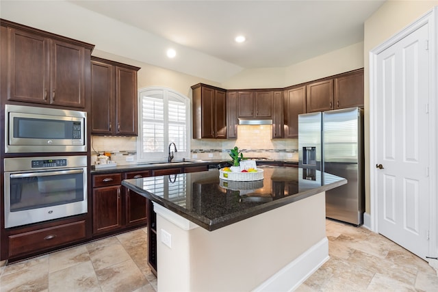 kitchen with vaulted ceiling, backsplash, stainless steel appliances, a center island, and dark stone counters