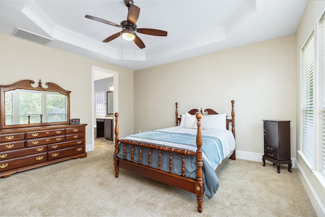 bedroom featuring light carpet, ensuite bath, a raised ceiling, crown molding, and ceiling fan