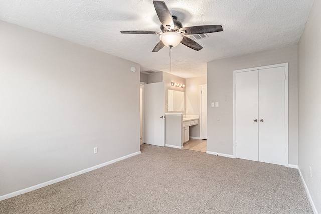 unfurnished bedroom featuring a closet, a textured ceiling, ceiling fan, ensuite bathroom, and light colored carpet