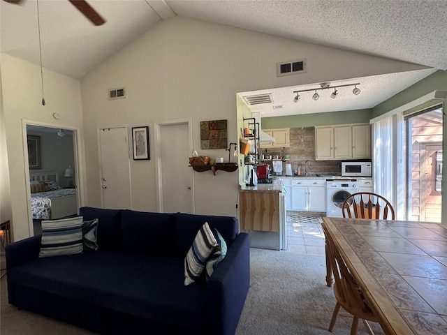 living room featuring ceiling fan, a textured ceiling, high vaulted ceiling, washer / dryer, and light colored carpet