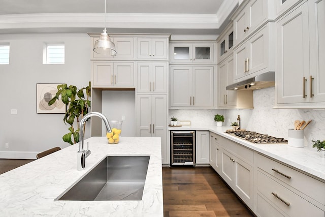 kitchen with sink, hanging light fixtures, ornamental molding, light stone countertops, and beverage cooler