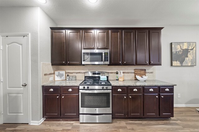 kitchen with light stone countertops, light hardwood / wood-style floors, appliances with stainless steel finishes, and dark brown cabinetry