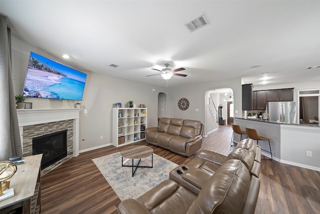 living room with ceiling fan, sink, dark wood-type flooring, and a stone fireplace