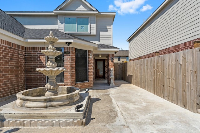 exterior space featuring fence, a shingled roof, and brick siding