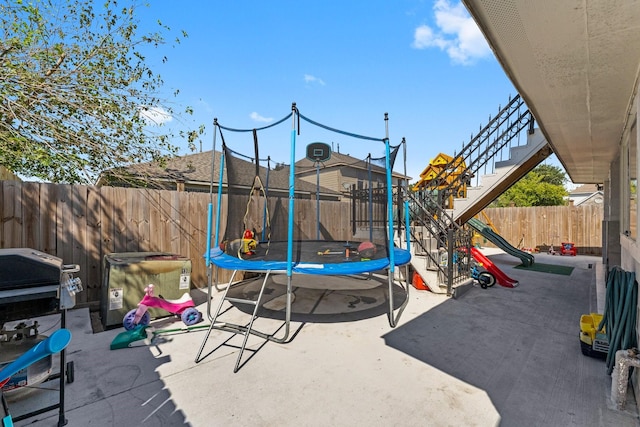 view of playground featuring a trampoline, a patio area, and a fenced backyard