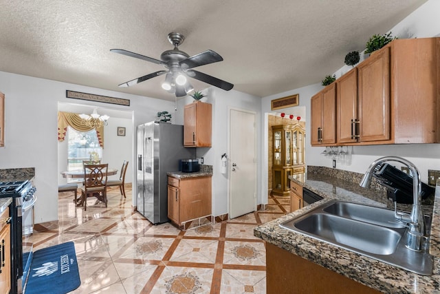 kitchen featuring stainless steel appliances, a sink, a textured ceiling, ceiling fan with notable chandelier, and brown cabinetry