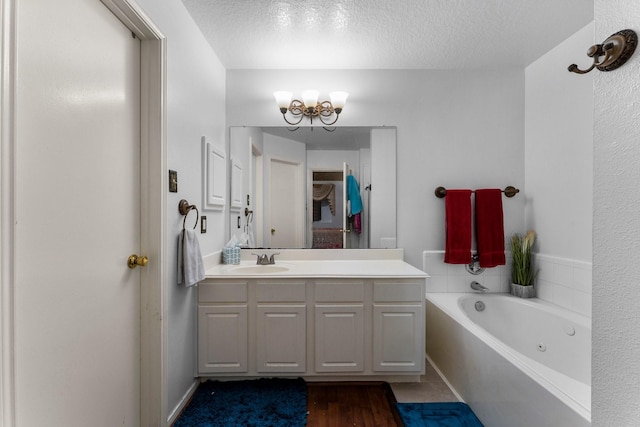 bathroom with a textured ceiling, a chandelier, wood finished floors, a whirlpool tub, and vanity