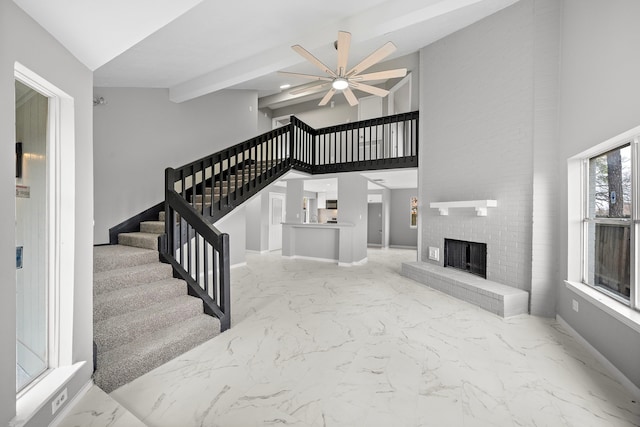 interior space featuring ceiling fan, a fireplace, beam ceiling, and a high ceiling