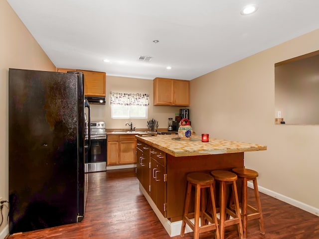 kitchen with a breakfast bar, a center island, dark hardwood / wood-style floors, black fridge, and stainless steel range