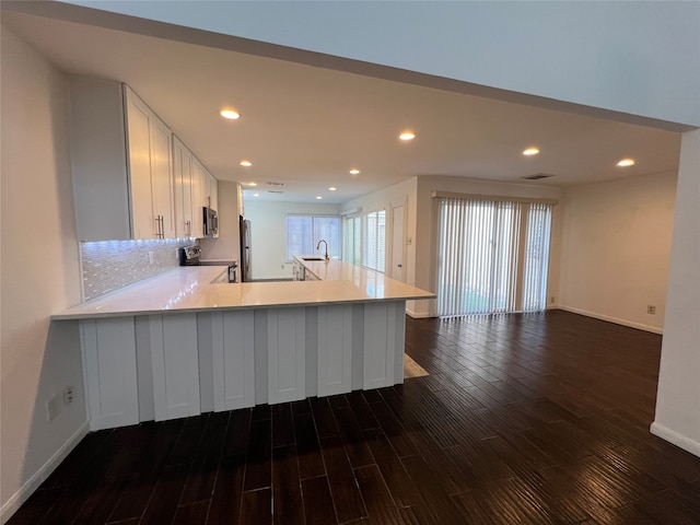 kitchen with appliances with stainless steel finishes, white cabinetry, dark wood-type flooring, kitchen peninsula, and sink