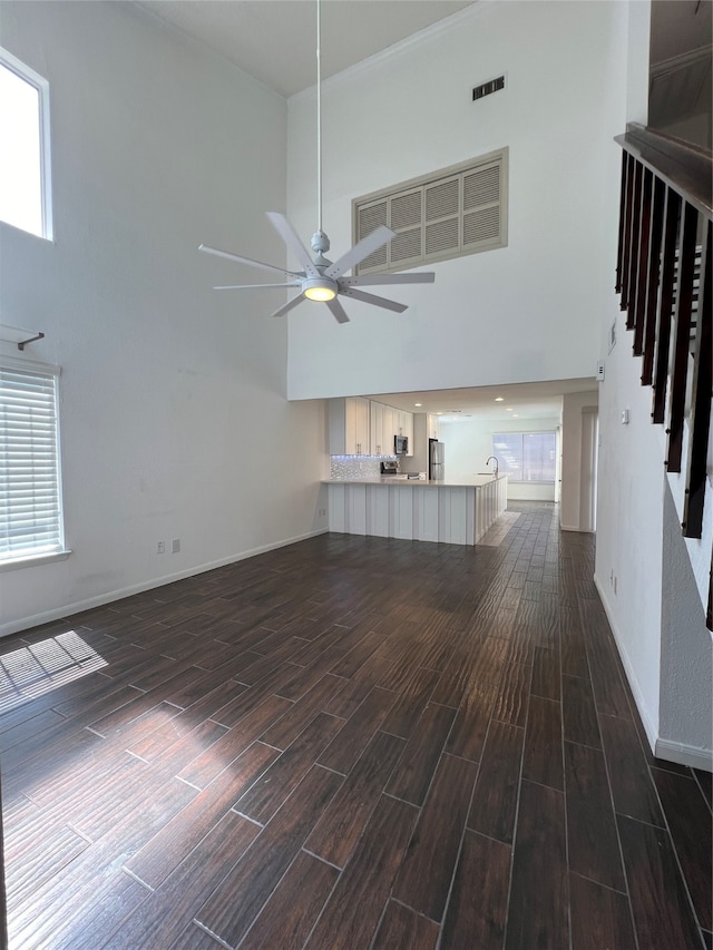 unfurnished living room with ceiling fan, a towering ceiling, and dark wood-type flooring