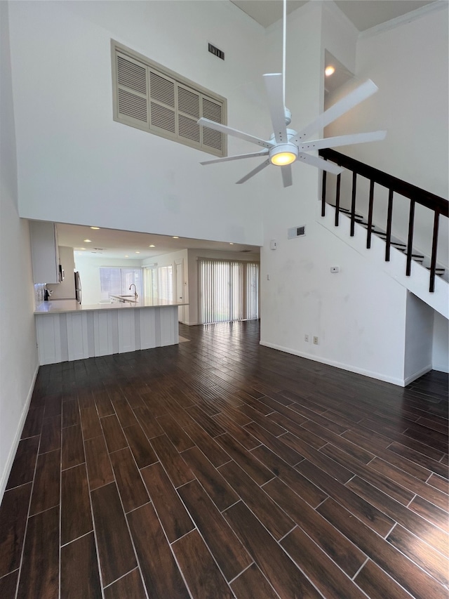 unfurnished living room with ceiling fan, a high ceiling, and dark hardwood / wood-style flooring