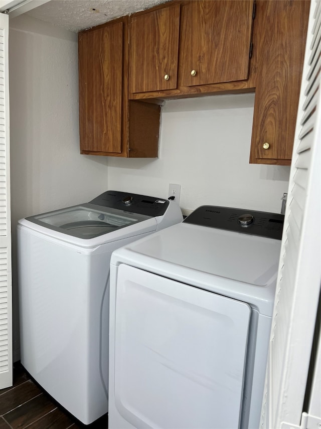 clothes washing area with a textured ceiling, dark hardwood / wood-style flooring, washer and dryer, and cabinets