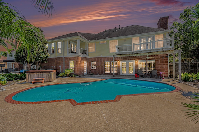 pool at dusk with a hot tub and a patio