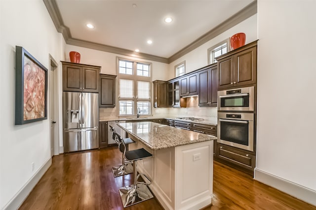 kitchen with sink, a center island, dark hardwood / wood-style floors, a kitchen bar, and appliances with stainless steel finishes