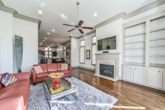 living room featuring ceiling fan with notable chandelier, hardwood / wood-style flooring, built in features, and ornamental molding