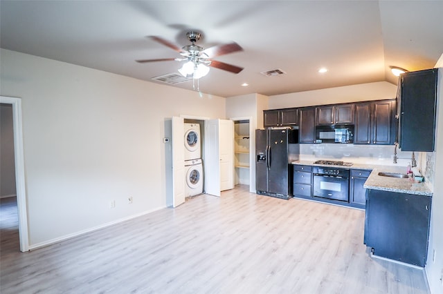 kitchen featuring ceiling fan, sink, stacked washer and clothes dryer, black appliances, and light wood-type flooring