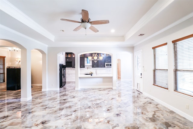 unfurnished living room with ceiling fan with notable chandelier, crown molding, and a raised ceiling