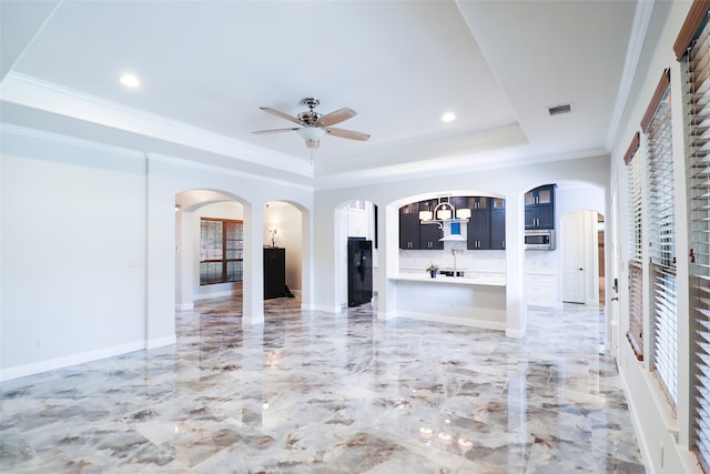 unfurnished living room with ceiling fan with notable chandelier, a tray ceiling, and ornamental molding