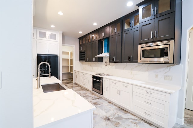 kitchen with sink, wall chimney range hood, white cabinetry, appliances with stainless steel finishes, and light stone countertops