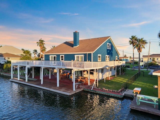 back house at dusk with a lawn and a water view