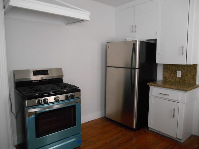 kitchen with white cabinets, ventilation hood, appliances with stainless steel finishes, dark stone countertops, and dark hardwood / wood-style flooring