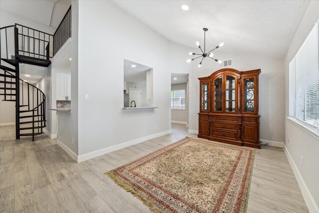 entryway with a notable chandelier, high vaulted ceiling, and light hardwood / wood-style flooring