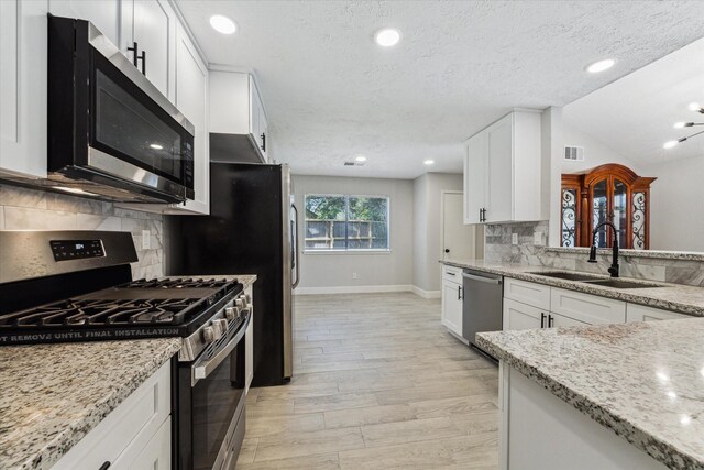 kitchen with light stone counters, lofted ceiling, sink, white cabinetry, and stainless steel appliances