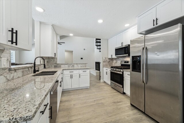 kitchen featuring appliances with stainless steel finishes, white cabinetry, light stone counters, light hardwood / wood-style flooring, and sink