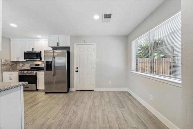 kitchen with decorative backsplash, light hardwood / wood-style floors, white cabinetry, light stone countertops, and stainless steel appliances