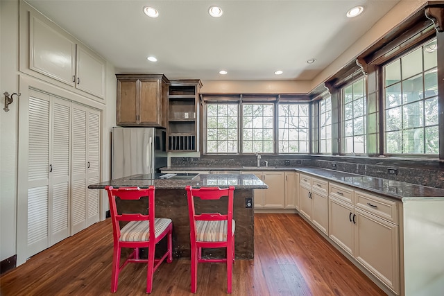 kitchen featuring stainless steel refrigerator, dark stone countertops, a kitchen island, and dark wood-type flooring