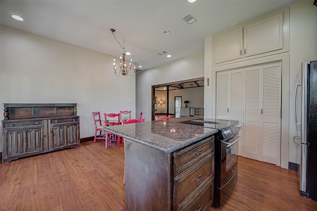 kitchen with dark brown cabinetry, dark stone counters, black / electric stove, stainless steel refrigerator, and light wood-type flooring