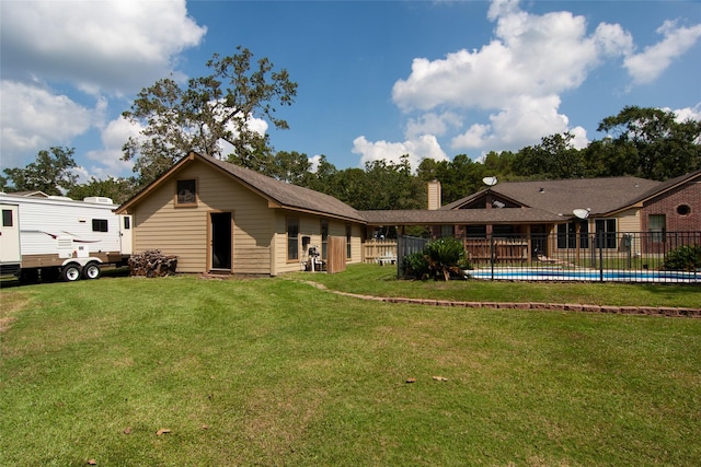 rear view of house with a lawn, a chimney, fence, and a fenced in pool