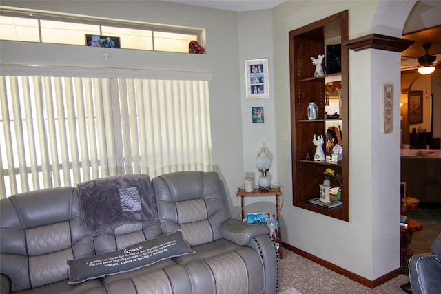 carpeted living room with arched walkways, built in features, baseboards, and ceiling fan