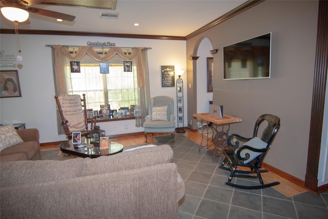 living area with crown molding, a ceiling fan, baseboards, visible vents, and arched walkways