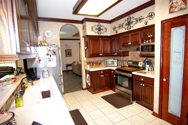 kitchen with light tile patterned floors, ornamental molding, sink, tasteful backsplash, and appliances with stainless steel finishes