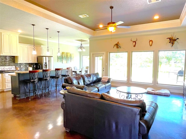 living room featuring ornamental molding, a textured ceiling, ceiling fan with notable chandelier, and a tray ceiling