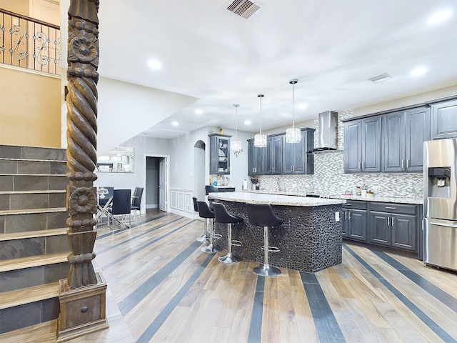 kitchen featuring light wood-type flooring, stainless steel fridge with ice dispenser, a kitchen bar, a kitchen island, and wall chimney exhaust hood