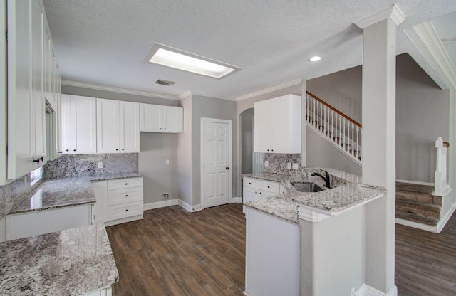 kitchen featuring light stone counters, kitchen peninsula, a textured ceiling, dark wood-type flooring, and white cabinetry